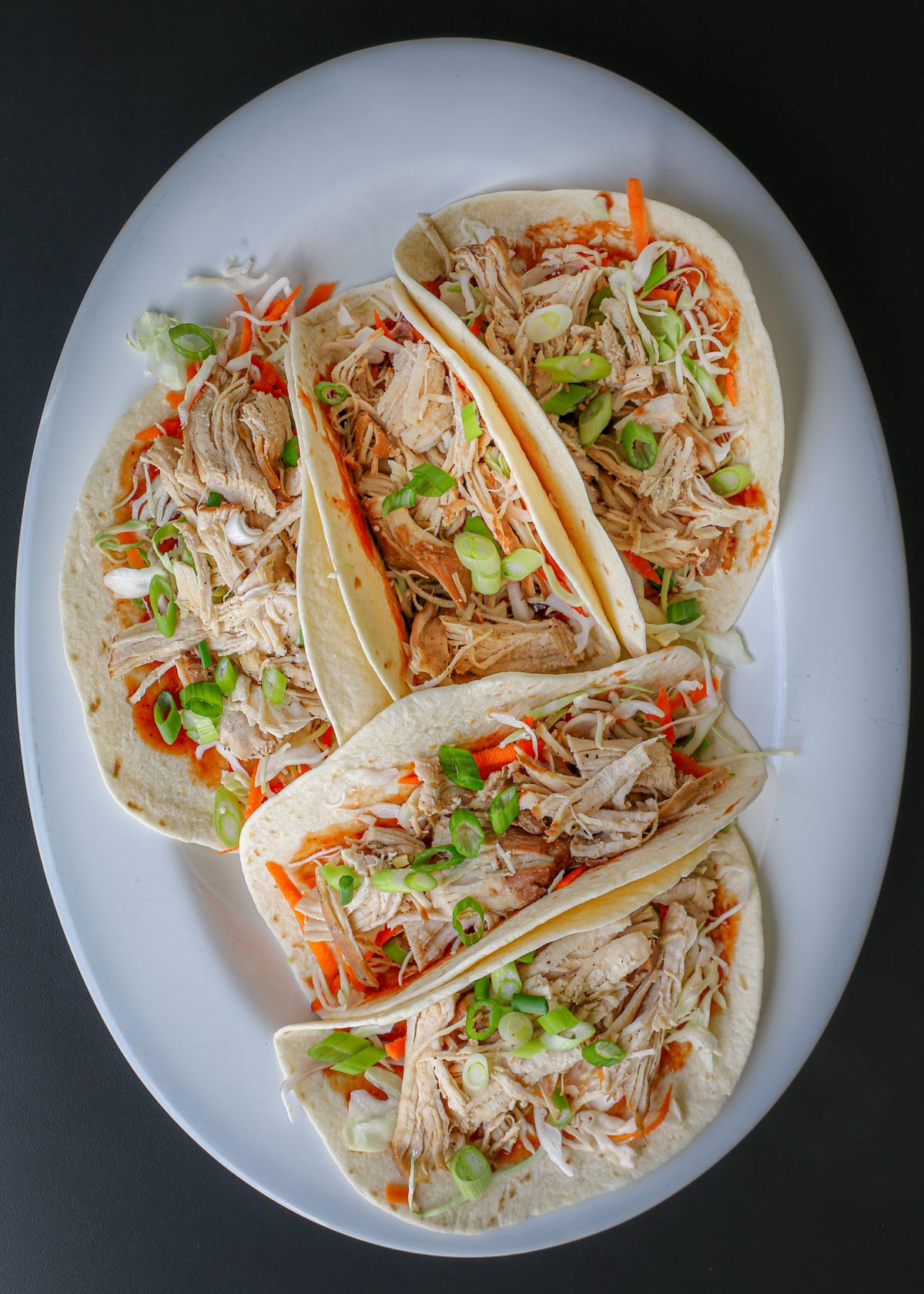 a platter of moo shu chicken on tortillas with toppings.