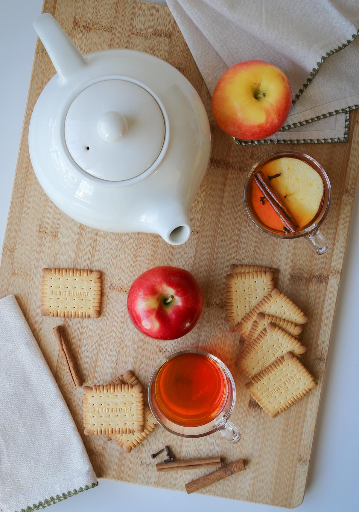 a spread of tea pot, cups, and cookies with apples and cinnamon sticks scattered about.