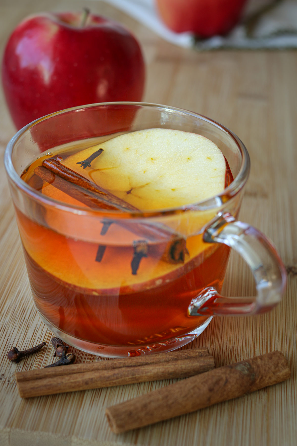 glass mug of apple cinnamon tea with apples and cinnamon sticks nearby.