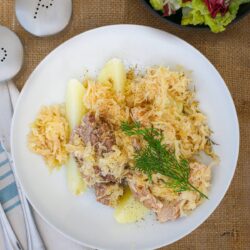 overhead shot of sauerkraut and pork on potatoes with dill garnish.