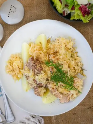 overhead shot of sauerkraut and pork on potatoes with dill garnish.