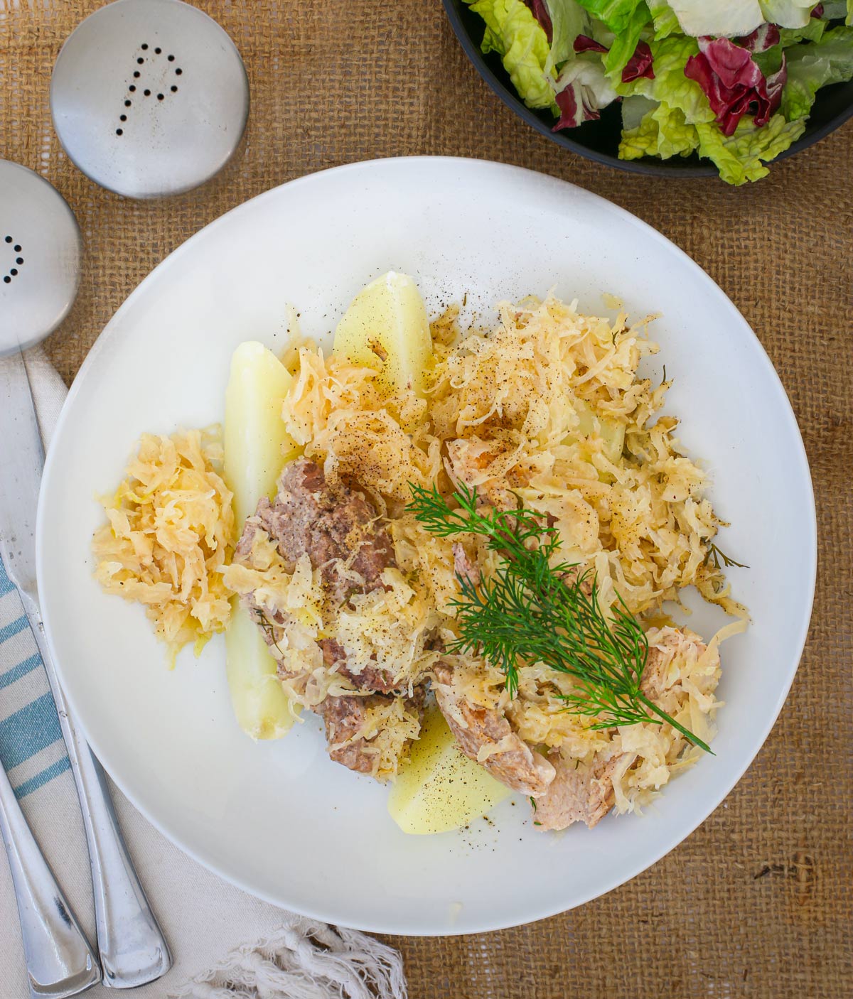 overhead shot of sauerkraut and pork on potatoes with dill garnish.