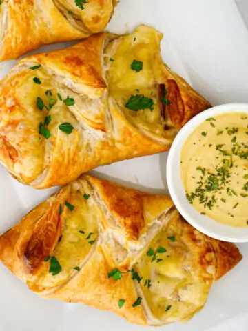 flatly of ham and cheese croissants on a white platter with dipping sauce.