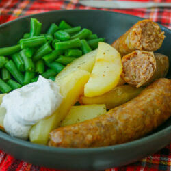 black plate of sausages, potatoes, green beans, and sour cream sauce.