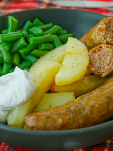 black plate of sausages, potatoes, green beans, and sour cream sauce.