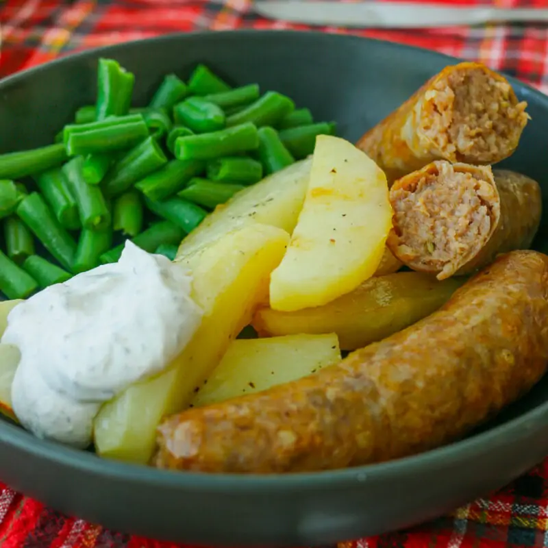 black plate of sausages, potatoes, green beans, and sour cream sauce.