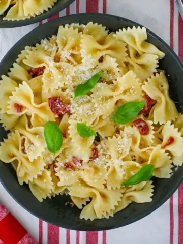 overhead shot of a bowl of brie and tomato pasta on red and white cloth.