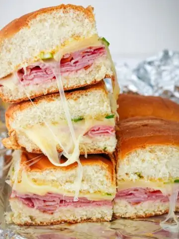 side view of stack of ham and cheese sliders on foil, with melty cheese.