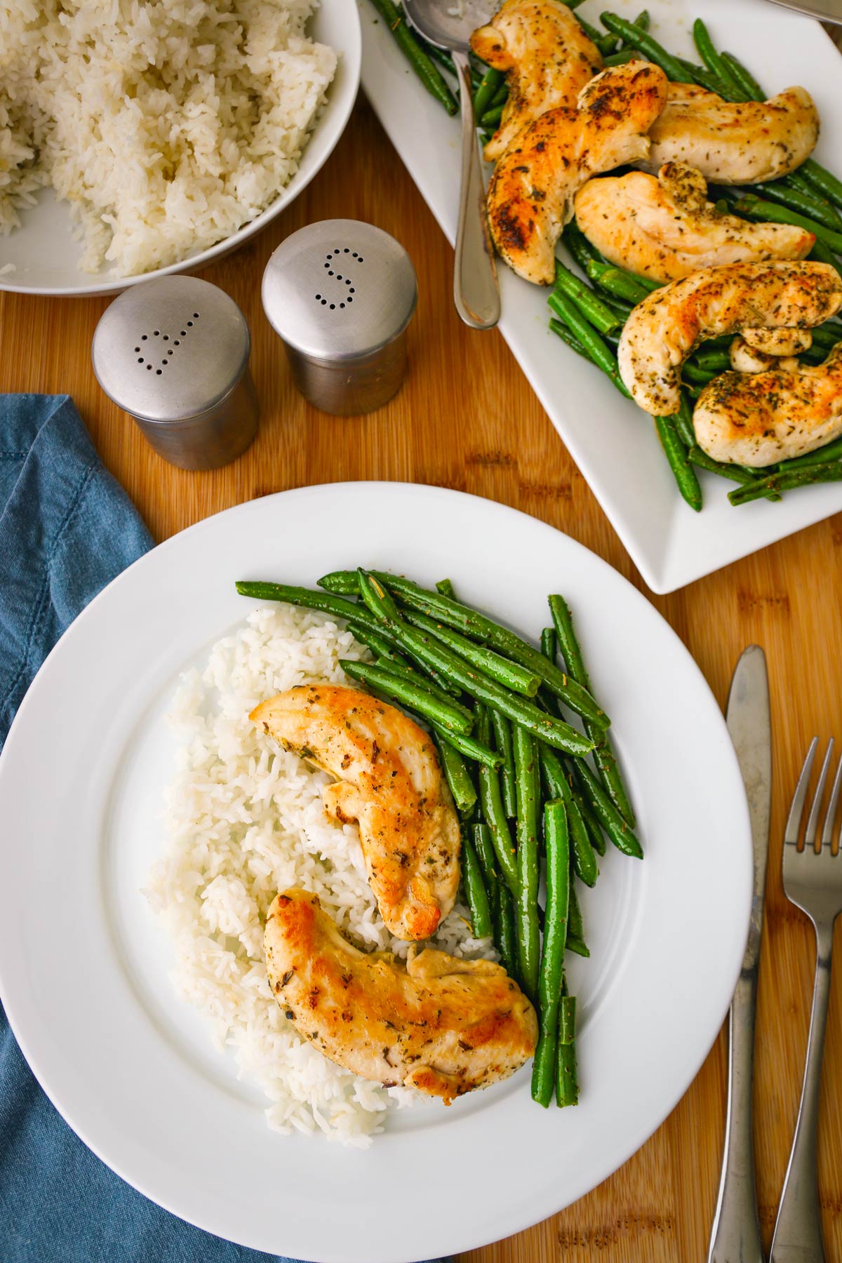 dinner table with plate of chicken and green beans with a platter and bowl of rice as well.