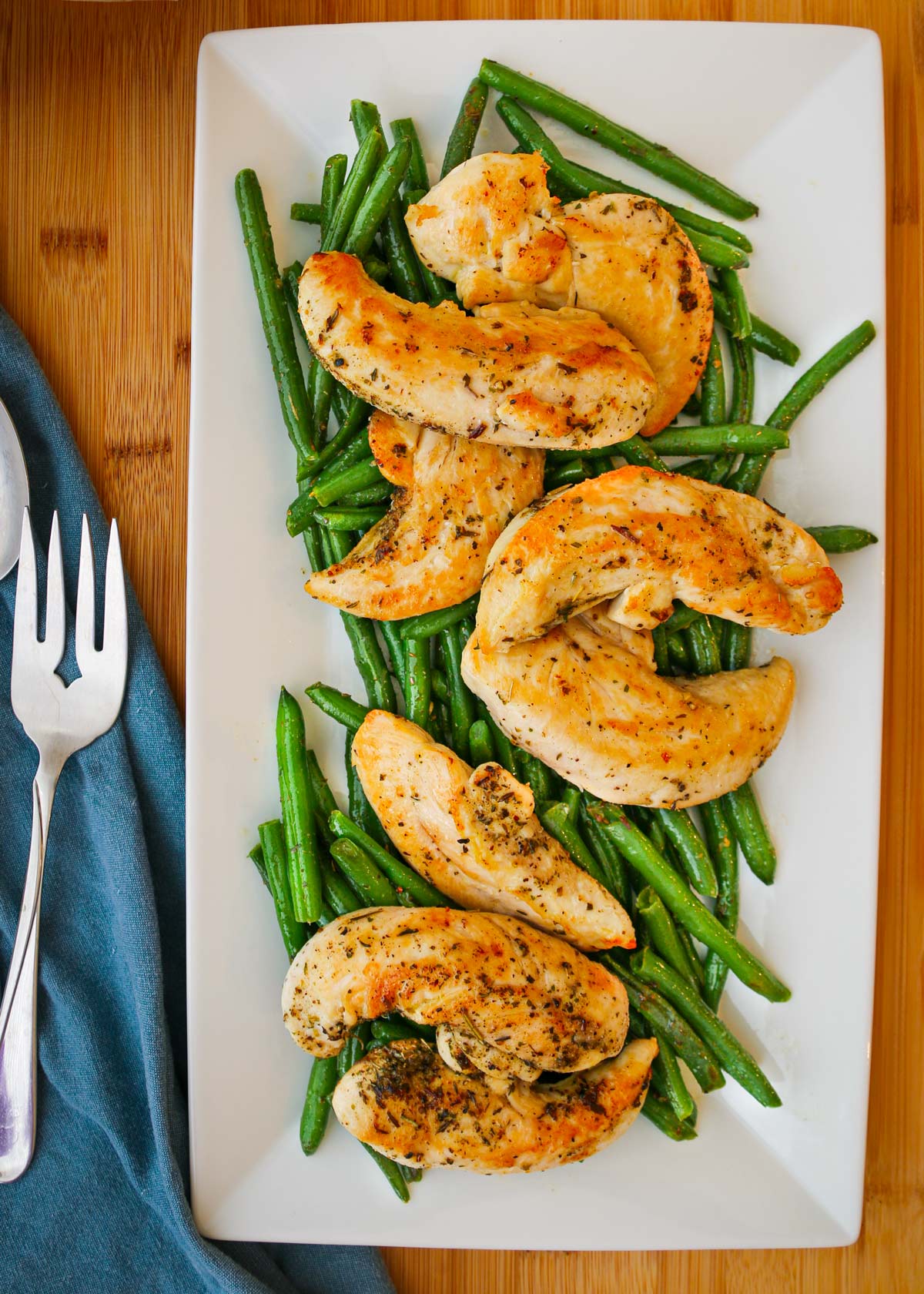 platter of green beans and chicken tenders on dinner table with napkin glad fork nearby.