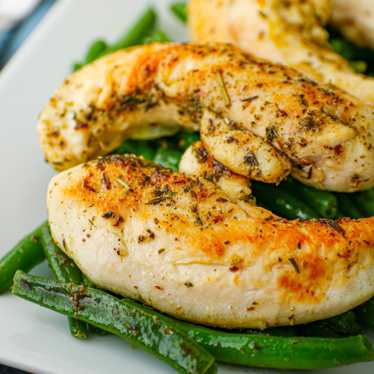 close up of chicken and green beans on white platter.