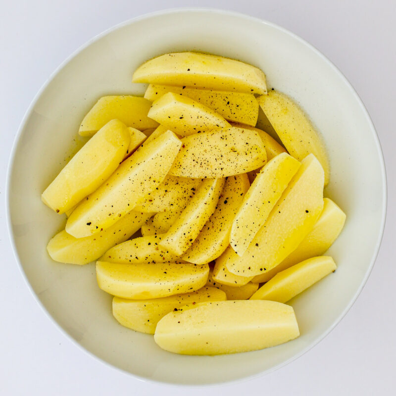 potatoes tossed in bowl with oil, salt, and pepper.