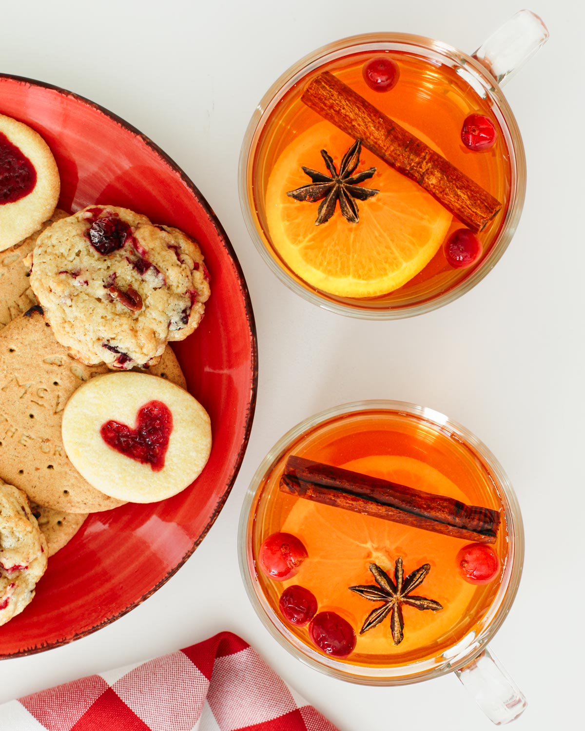 glass cups of wassail punch with garnishes and a plate of cookies.