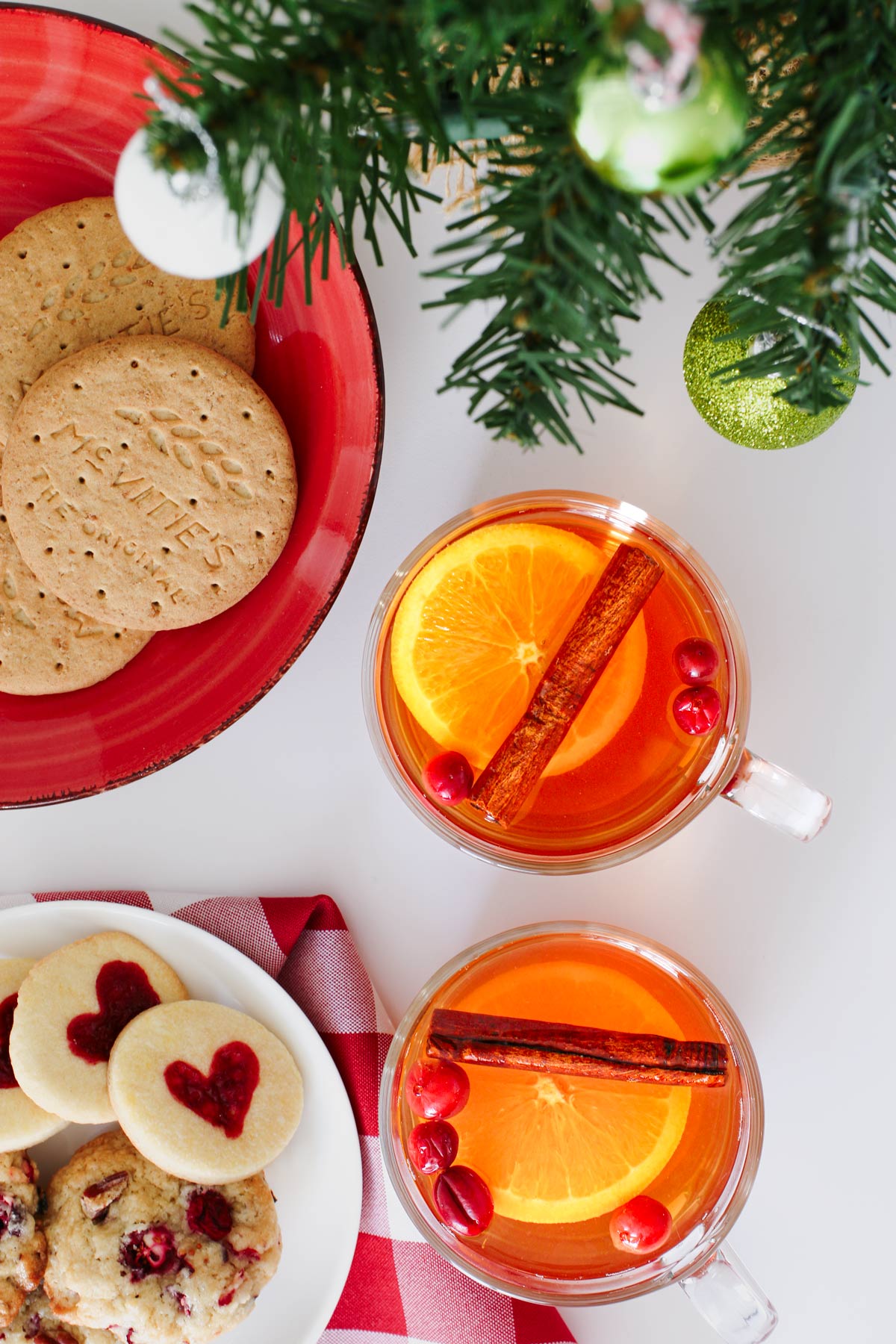 cookie plates and cups of wassail near a mini christmas tree on a white table.