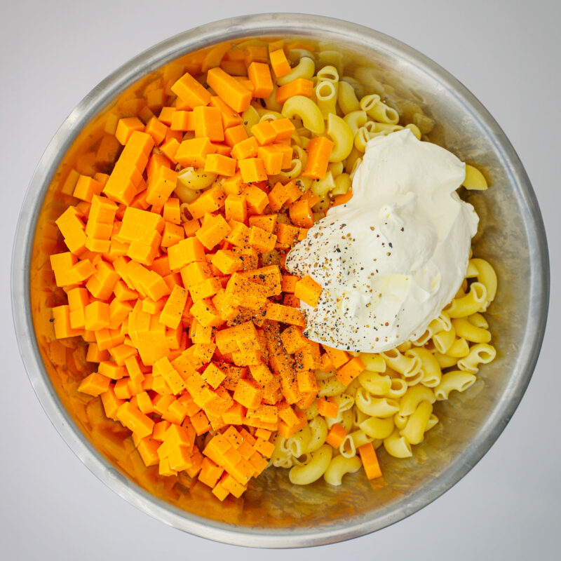 boiled noodles in a large bowl with sour cream, cheddar cheese, salt, and pepper.