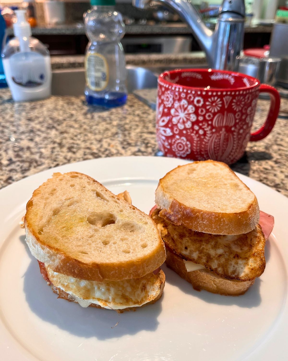 two small breakfast sandwiches on a white plate in front of the kitchen sink.