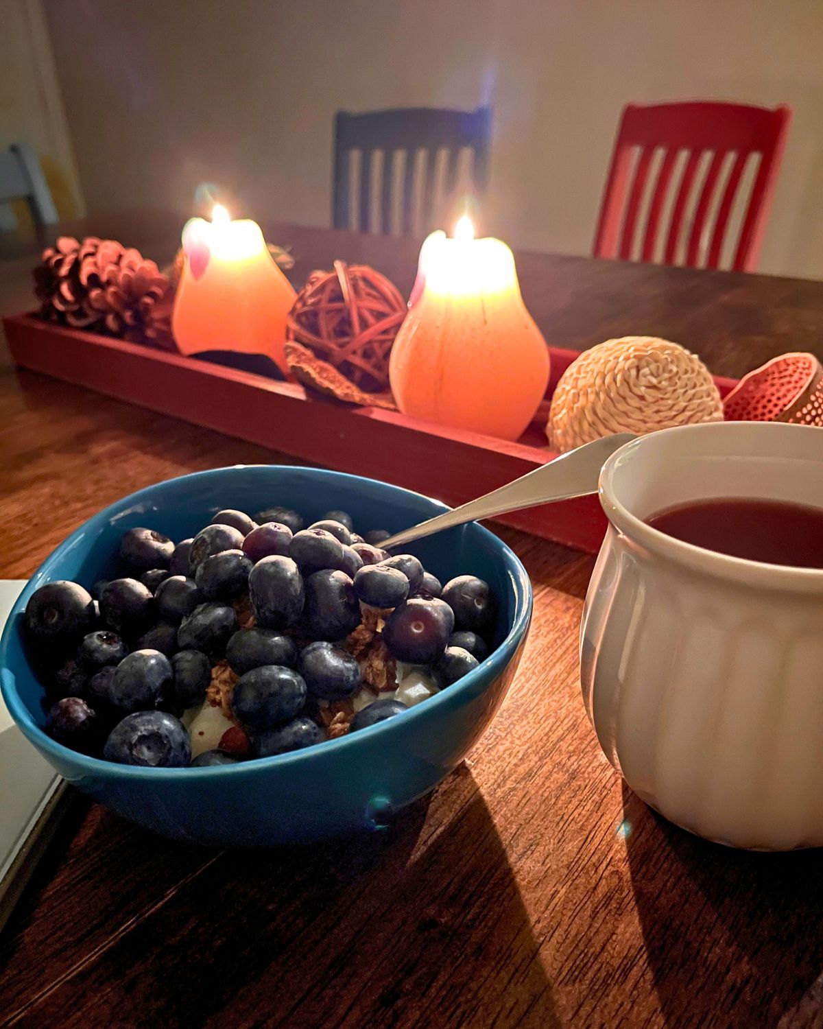 candlelight behind a bowl of blueberries and cup of tea.