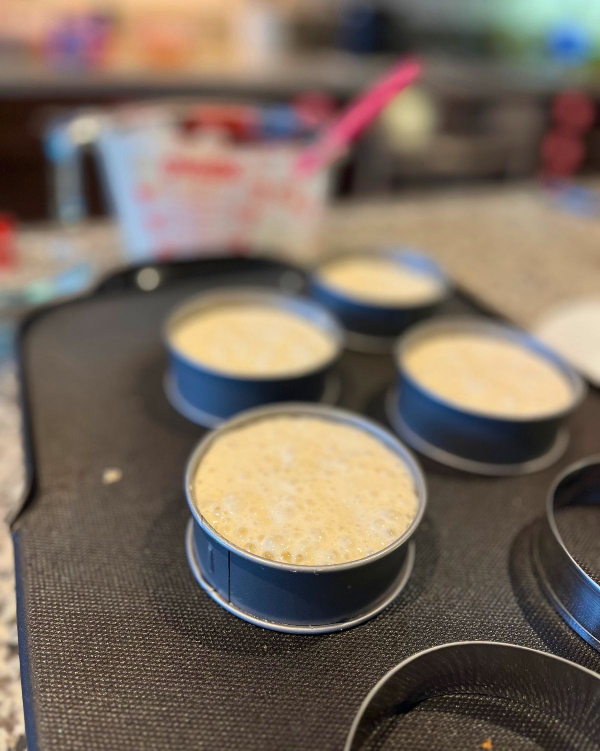 crumpets cooking on griddle in their metal rings.