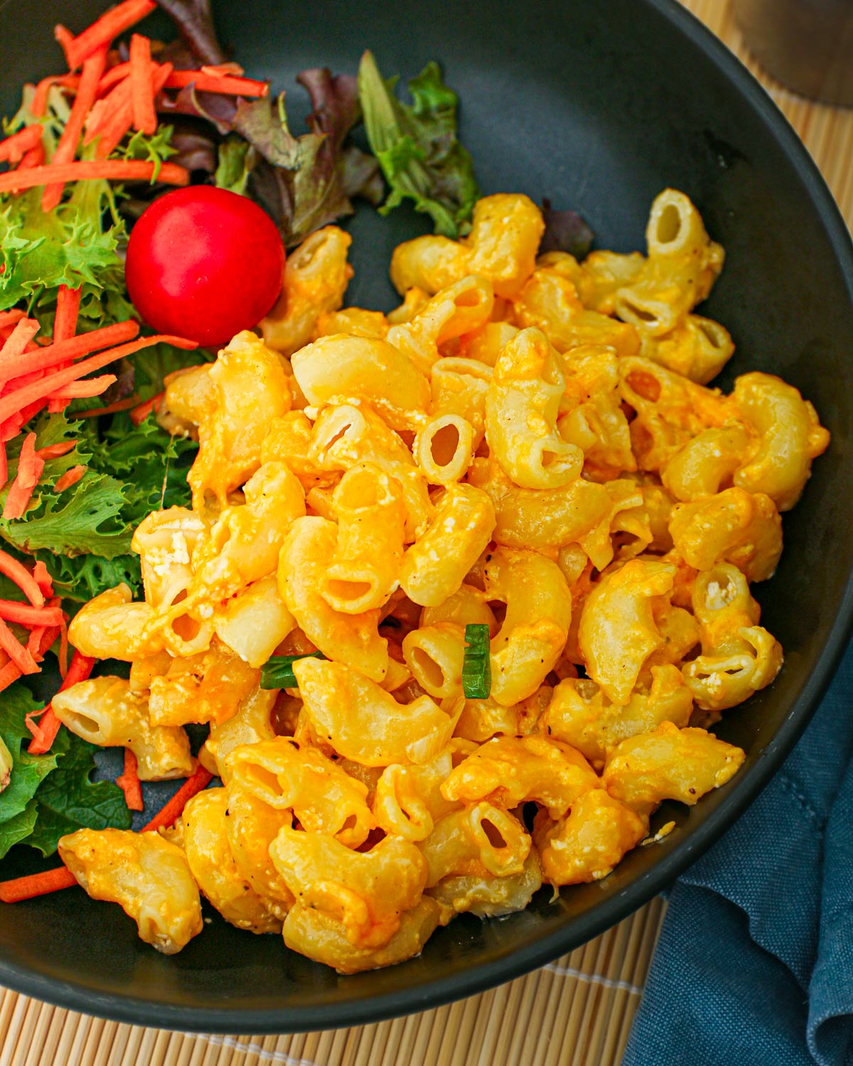 Mac and cheese on a black plate with a side salad.