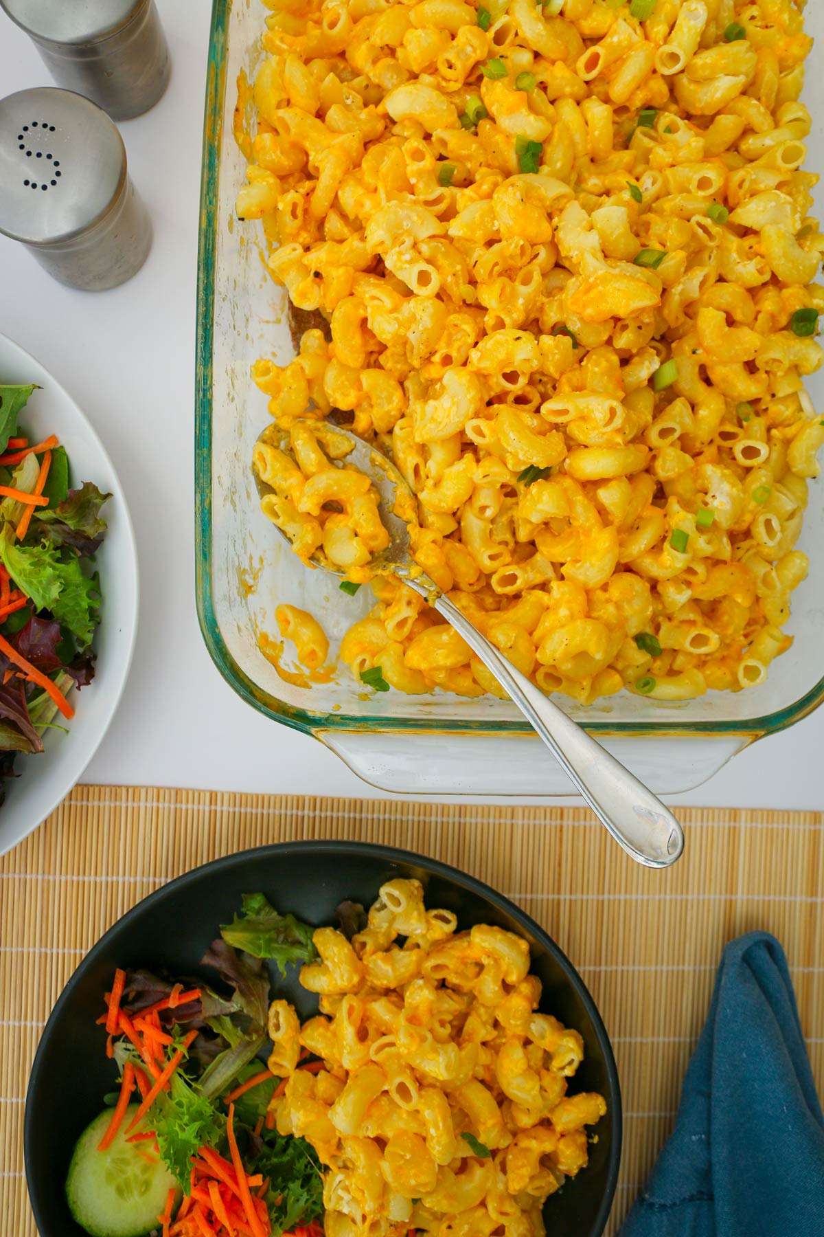 pan of Mac and cheese next to bowl of salad and a prepared dinner plate.