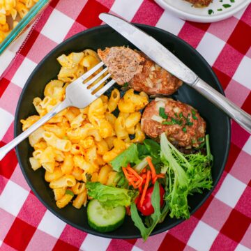 bite of mini meatloaf on a fork on a plate with mac and cheese and green salad.