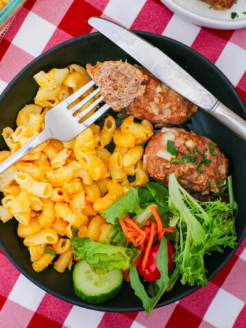 bite of mini meatloaf on a fork on a plate with mac and cheese and green salad.