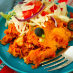 close up of crockpot enchiladas on a blue plate with fork and salad.