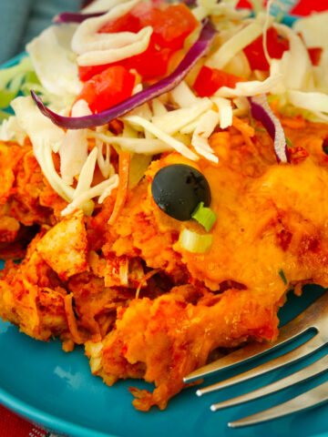 close up of crockpot enchiladas on a blue plate with fork and salad.