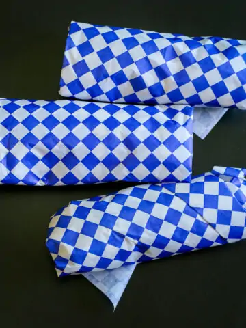 three freezer burritos wrapped in blue checked paper on black table.