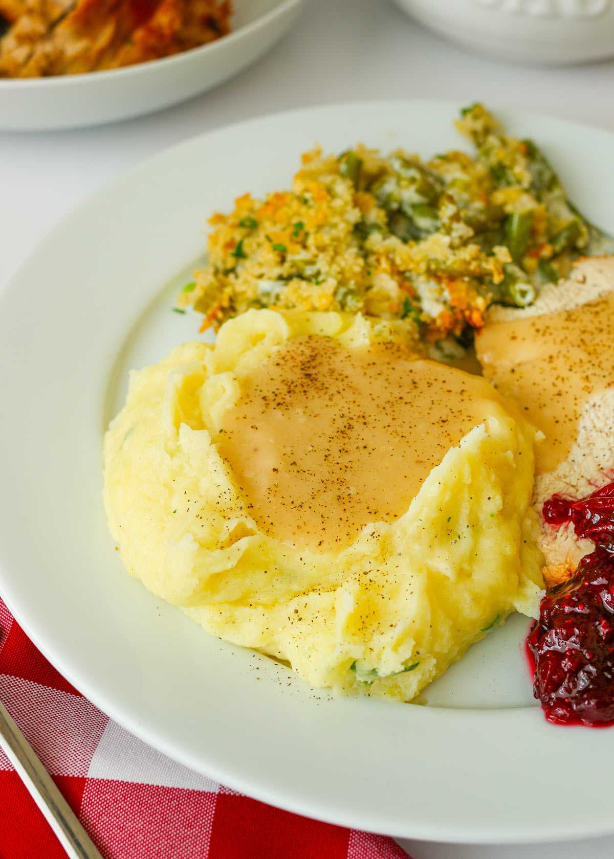 dinner plate with mashed potatoes and gravy as well as green bean casserole, turkey, and cranberry sauce.