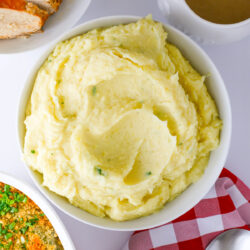 alfredo mashed potatoes in a white bowl on a dinner table surrounded by other dishes.