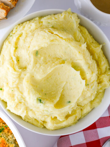 alfredo mashed potatoes in a white bowl on a dinner table surrounded by other dishes.