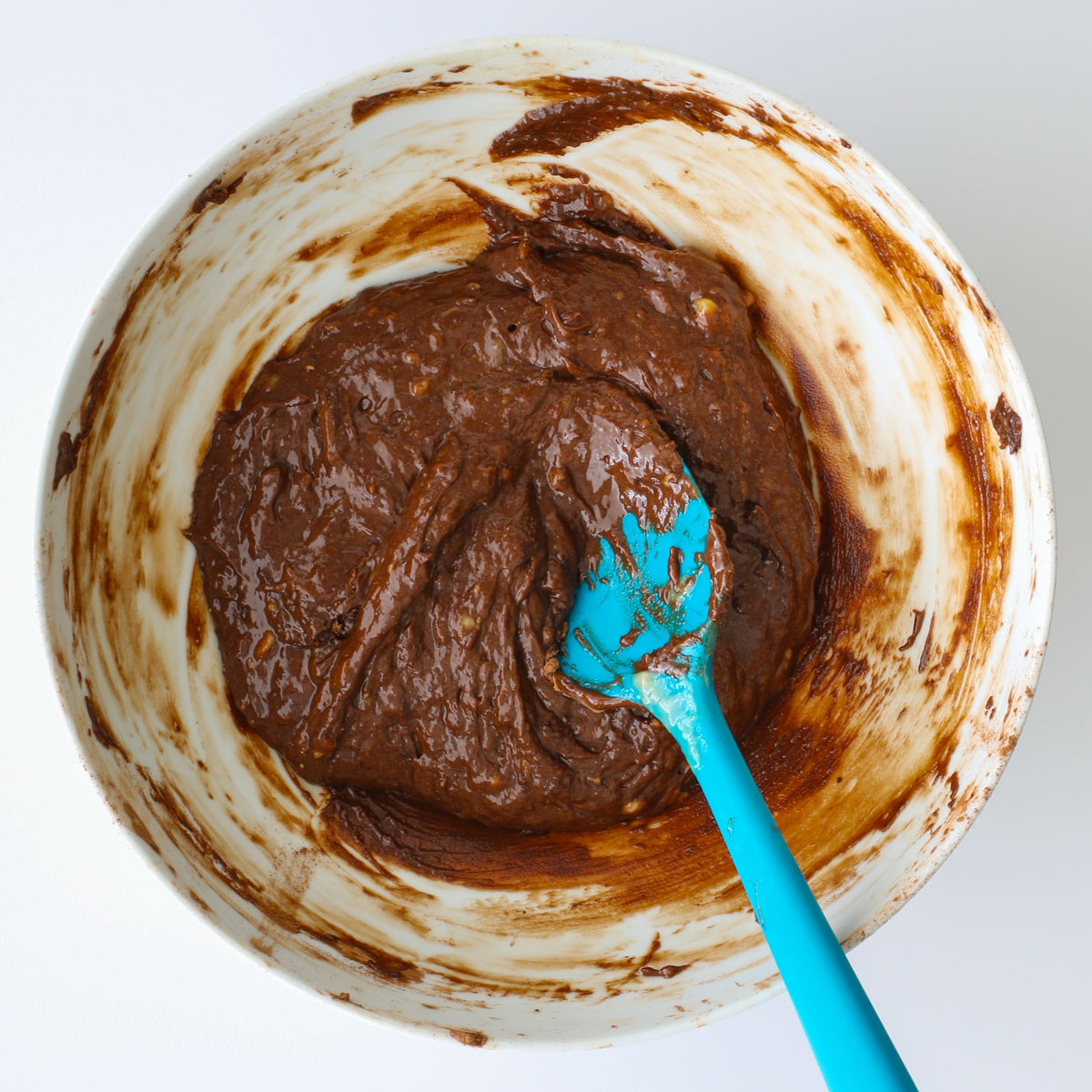 the chocolate batter stirred with a teal spatula in the white bowl.