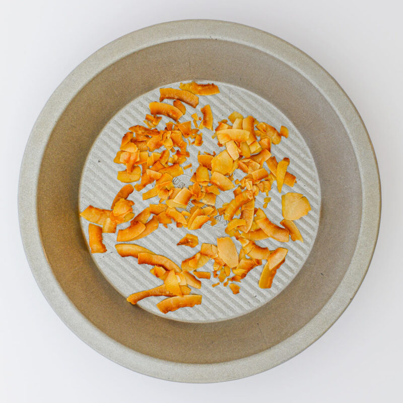 toasted coconut chips in pie plate on white table.