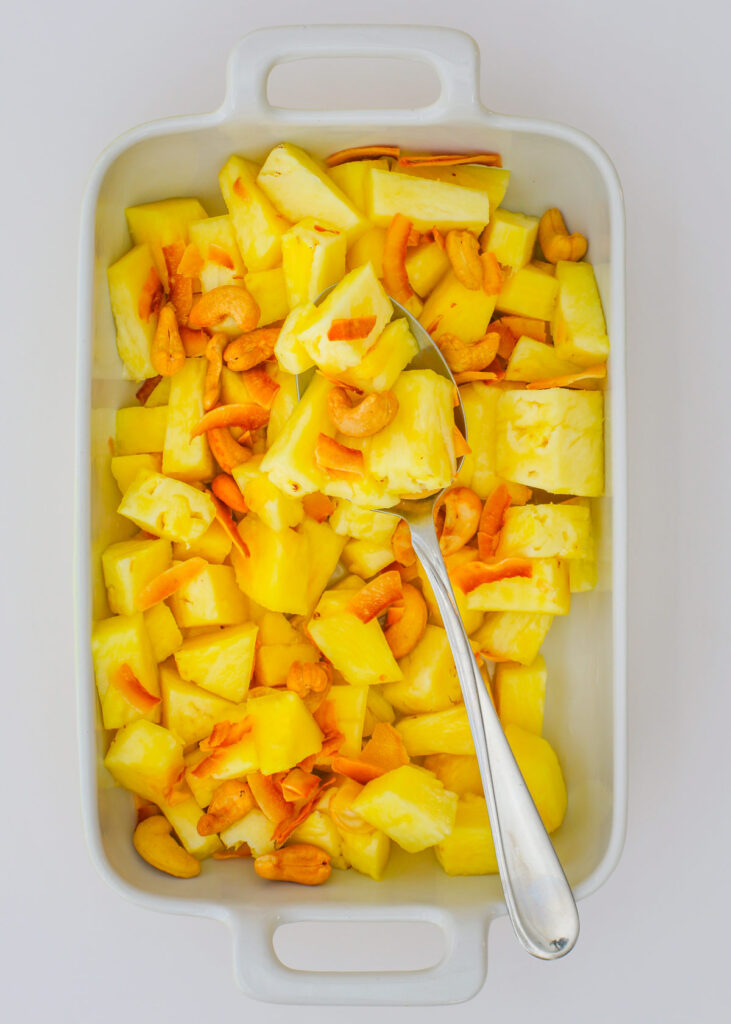 pineapple chunks in dish, topped with nuts and coconut, with a spoon to dish it out.