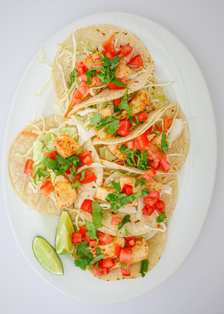 tomatoes and cilantro atop the fish tacos on platter.