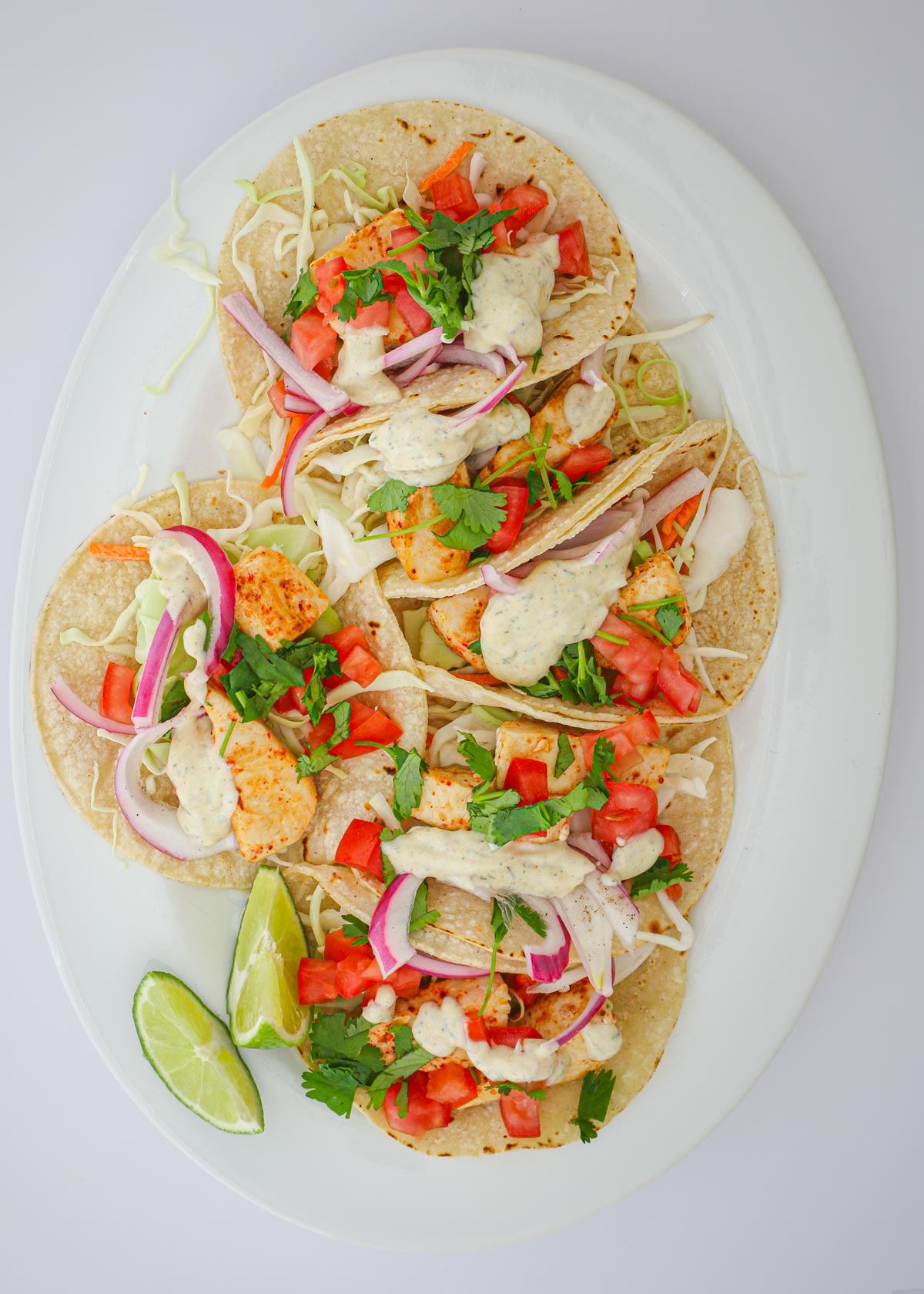 crema drizzled over fish tacos on platter.