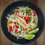 black dish with two mahi mahi fish tacos and two lime wedges.