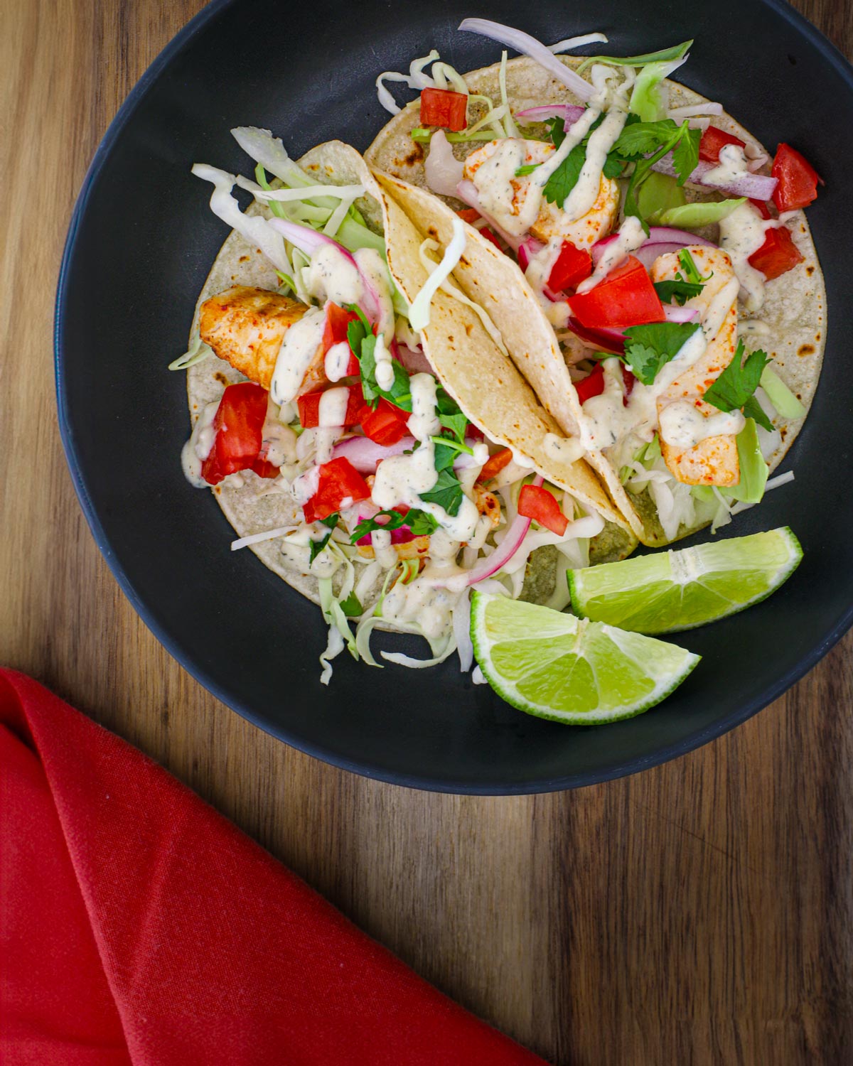 black plate of fish tacos on wooden surface with red napkin.