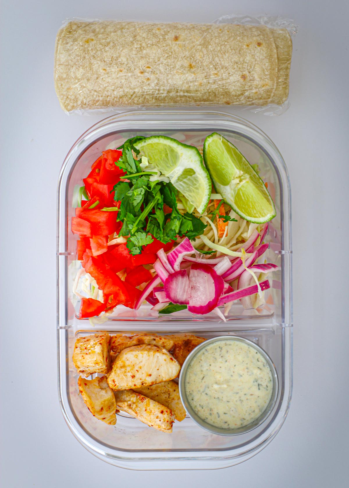 meal prep box with fish and crema in one section and toppings in another, wrapped tortillas are on the side.
