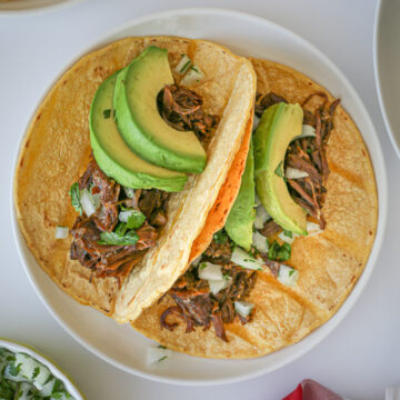 taco beef tacos topped with avocado on a white plate.