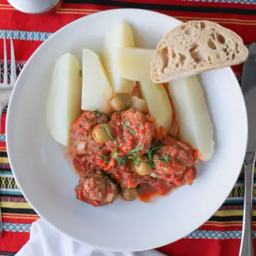 overhead shot of white bowl with potatoes and meatballs and slice of baguette.