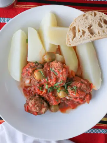 overhead shot of white bowl with potatoes and meatballs and slice of baguette.