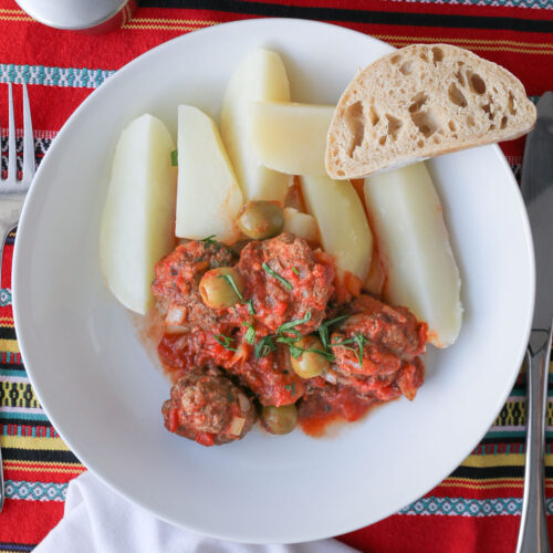 overhead shot of white bowl with potatoes and meatballs and slice of baguette.