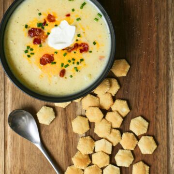scattered oyster crackers on a board next to a bowl of soup, with a spoon.
