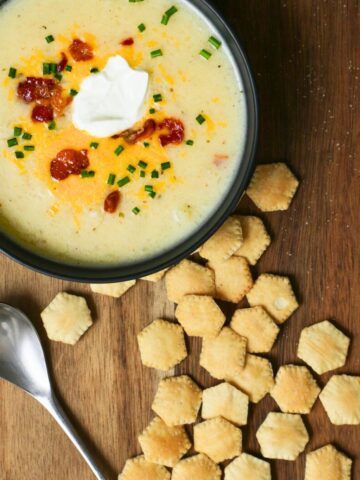 scattered oyster crackers on a board next to a bowl of soup, with a spoon.