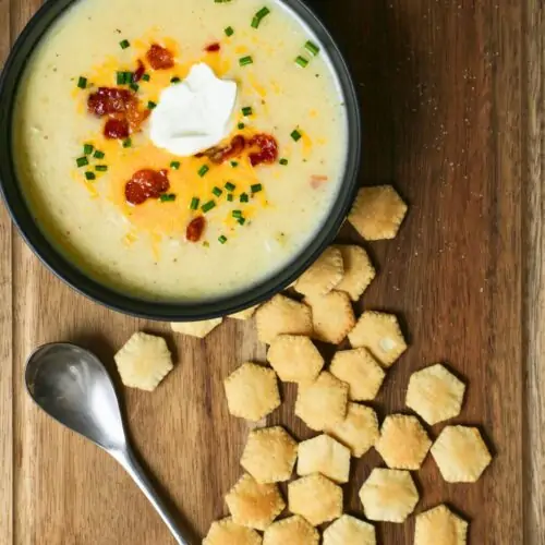 scattered oyster crackers on a board next to a bowl of soup, with a spoon.