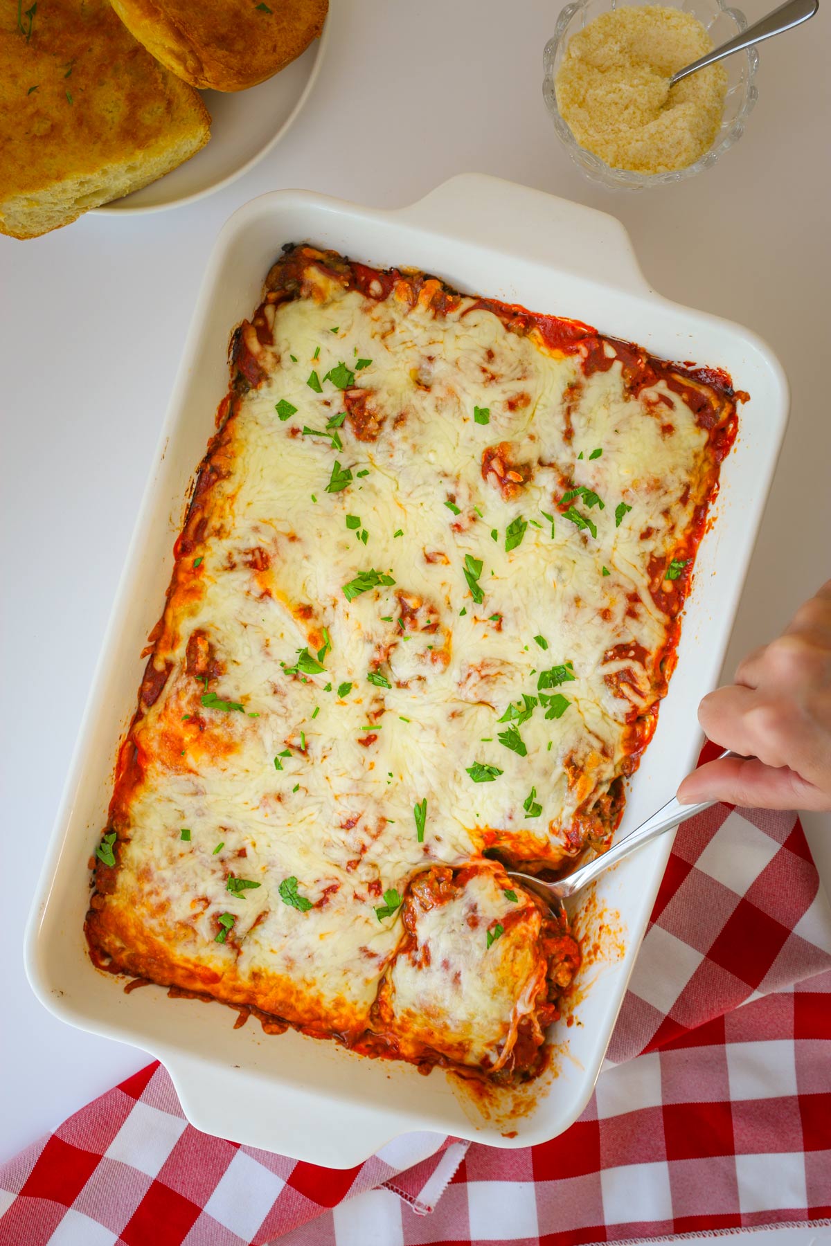 table set with ravioli casserole, garlic bread, and bowl of parmesan.