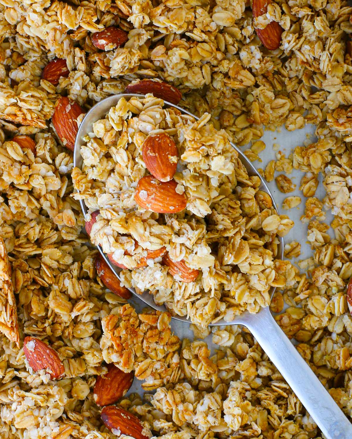 vanilla almond granola on baking sheet, scooped up in a large spoon.