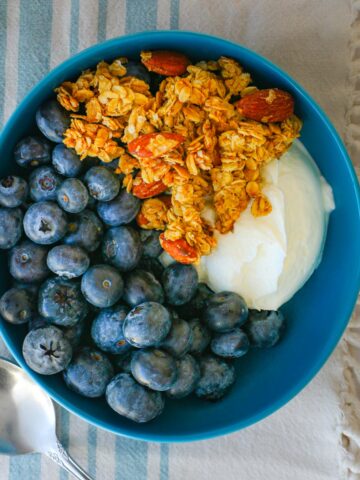 vanilla almond granola atop a yogurt and blueberry bowl.